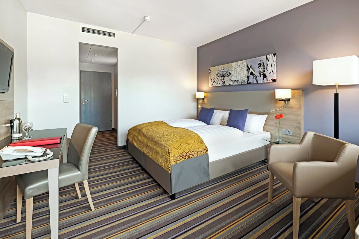 Een hotelkamer met een bed, een bureau met telefoon, een stoel, een lamp en een schilderij aan de muur.