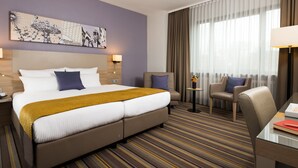 Ein Hotelzimmer mit einem großen Bett, zwei Sesseln, einem kleinen Tisch mit Blumenvase und einem Gemälde an der Wand.