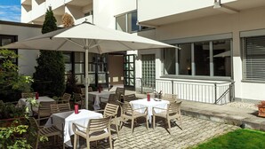 Eine Terrassensitzgruppe mit Tischen, Stühlen, einem großen Sonnenschirm und einem Blumentopf.