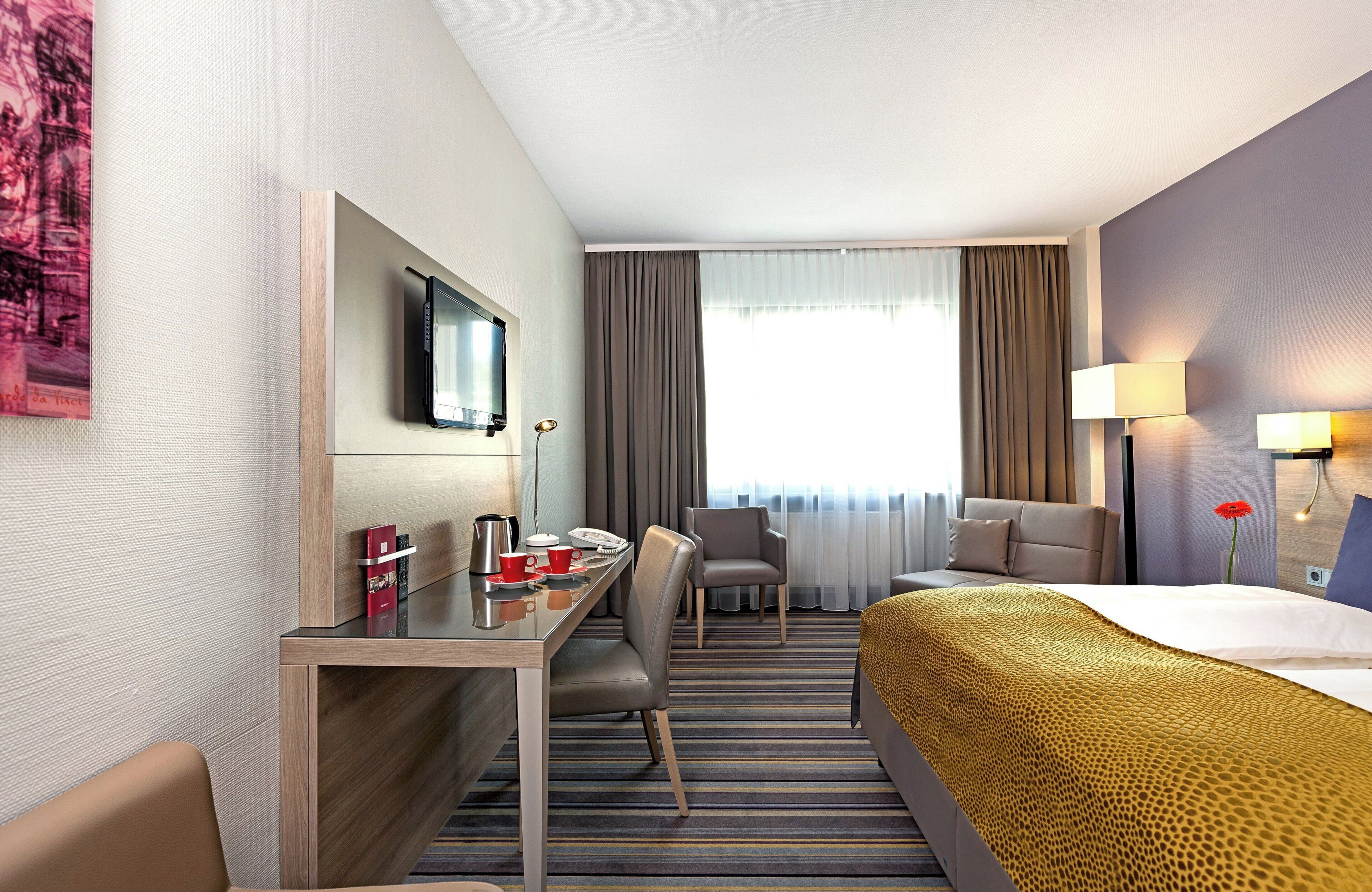 A hotel room with a bed, a desk with a chair, a television, and a window with curtains.