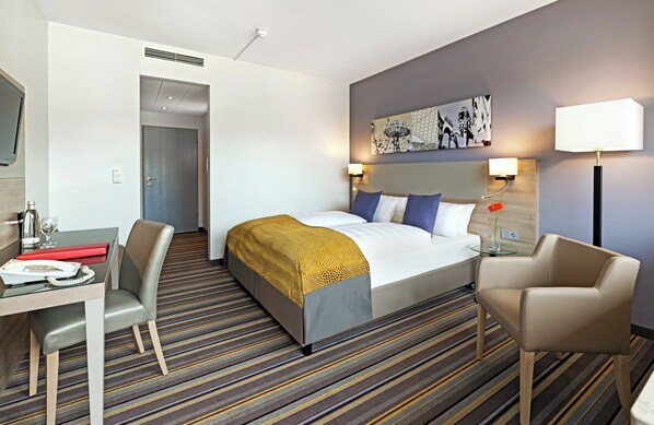 Une chambre d’hôtel avec un lit, un bureau avec un téléphone, une chaise, une lampe et un tableau au mur.