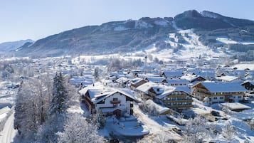 Ein verschneites Dorf mit traditionellen Chalets, einem Berg im Hintergrund und klarem Himmel.