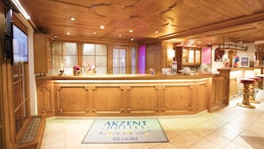 A spacious hotel lobby with wooden paneling, a large reception desk, and a sign indicating a 25-year anniversary. - AKZENT Hotel Alpenrose (Nesselwang)
