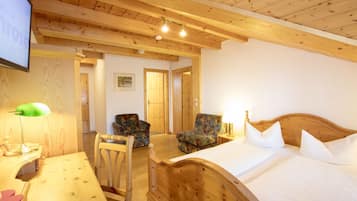 Ein Zimmer mit Holzboden, einem Bett, zwei Stühlen, einem Schreibtisch und einem Fernseher.