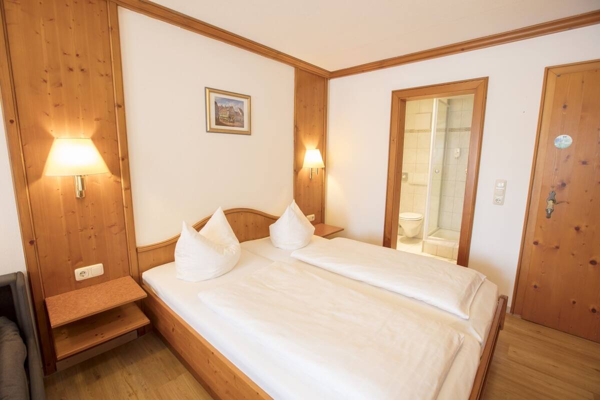 A double bed with white linens, two bedside lamps, a wooden headboard, a small bedside table, and a framed picture on the wall.