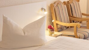 A neatly made bed with white linens, a bedside lamp, and a small vase with a flower. - AKZENT Hotel Alpenrose (Nesselwang)