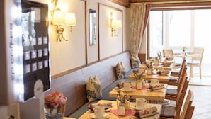 A restaurant with wooden tables and benches, wall-mounted lamps, and a large window with curtains. - AKZENT Hotel Alpenrose (Nesselwang)
