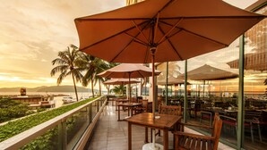 A terrace with wooden tables and chairs, large umbrellas, and a view of the ocean and mountains. - The Pacific Sutera Hotel (Kota Kinabalu)