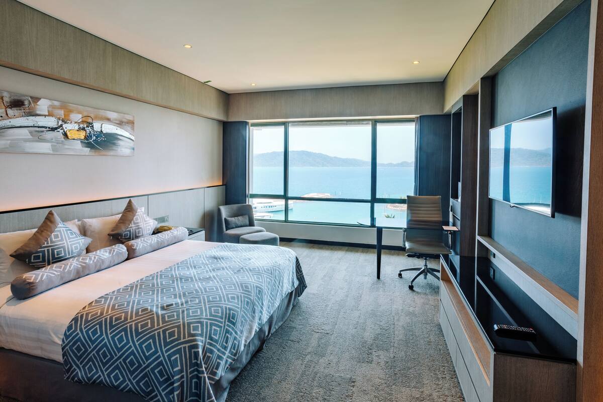 A modern hotel room with a large bed, a desk, a chair, and a TV.