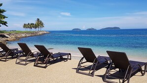 A beach with lounge chairs facing the ocean, palm trees, and distant islands. - The Pacific Sutera Hotel (Kota Kinabalu)