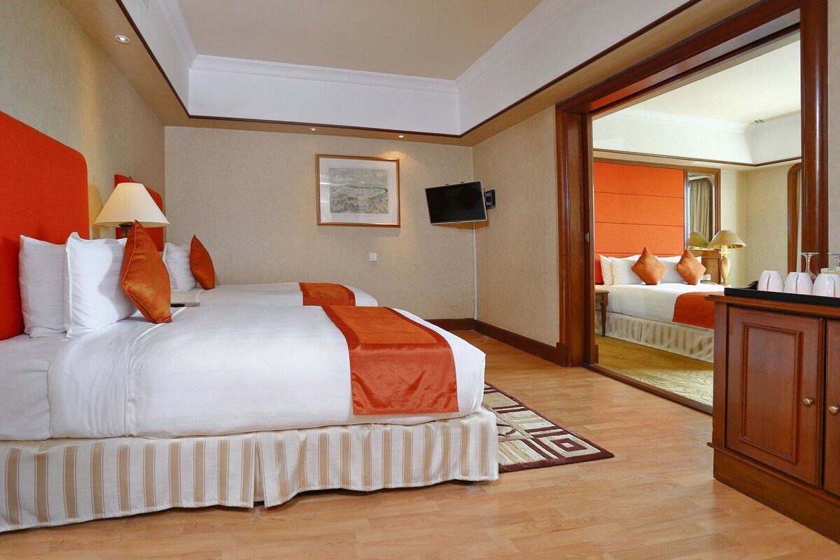 A hotel room with a large bed, a television, a mirror, and a wooden cabinet.