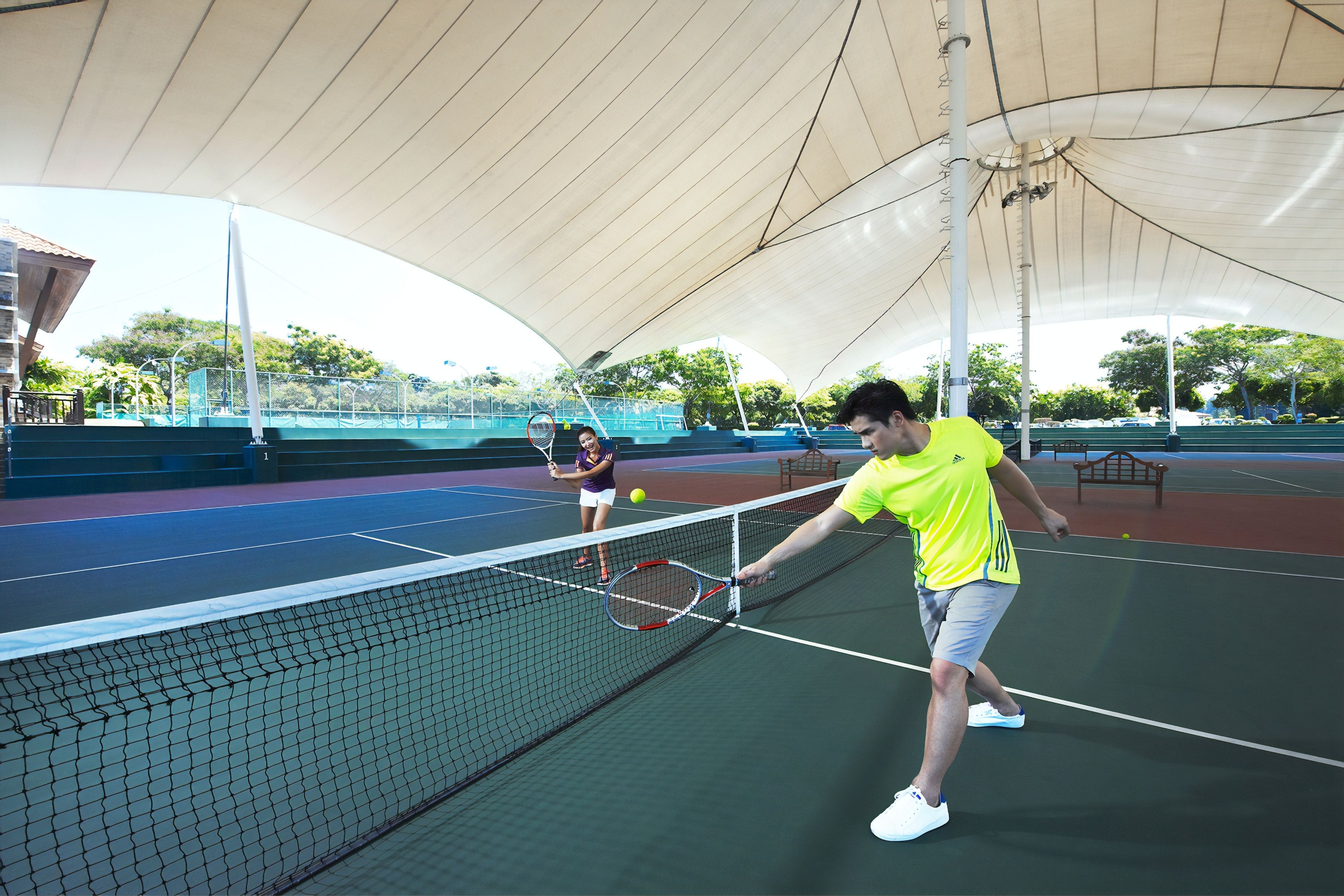 Ein Tennisplatz mit Netz, ein Spieler in einem gelben T-Shirt und ein weiterer Spieler in einem violetten T-Shirt.
