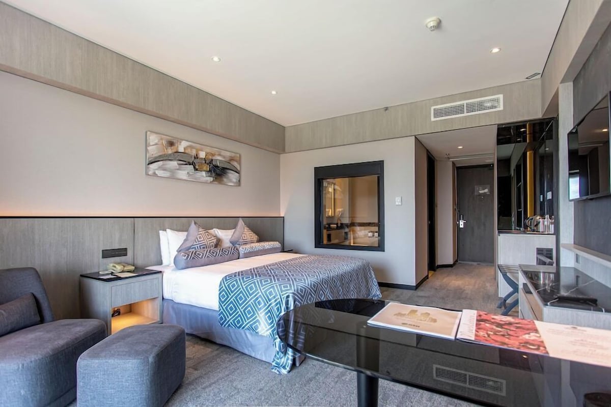 A modern hotel room with a bed, a desk, a chair, a sofa, and a large mirror.