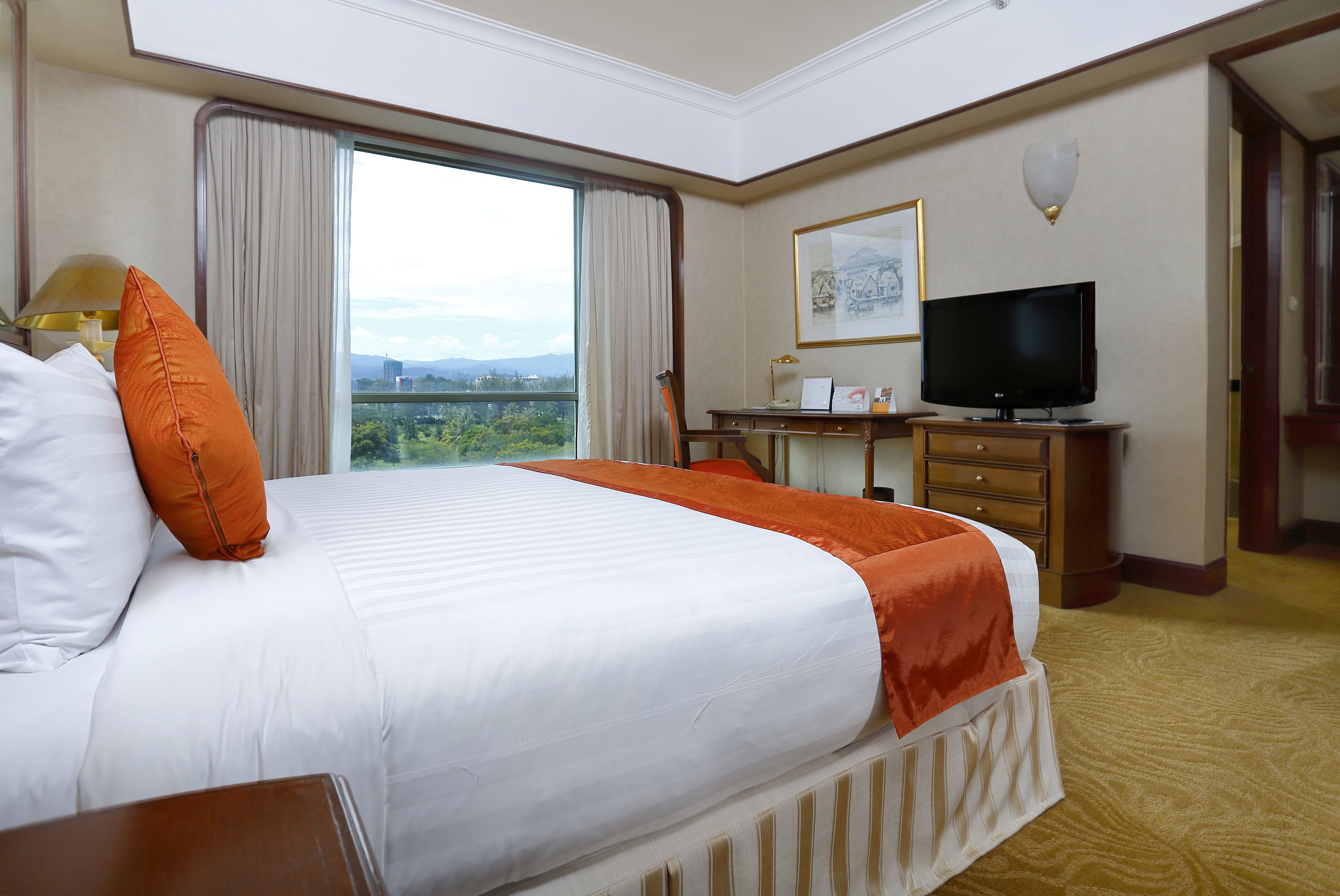 A hotel room with a large bed, a desk with a television, and a window offering a city view.