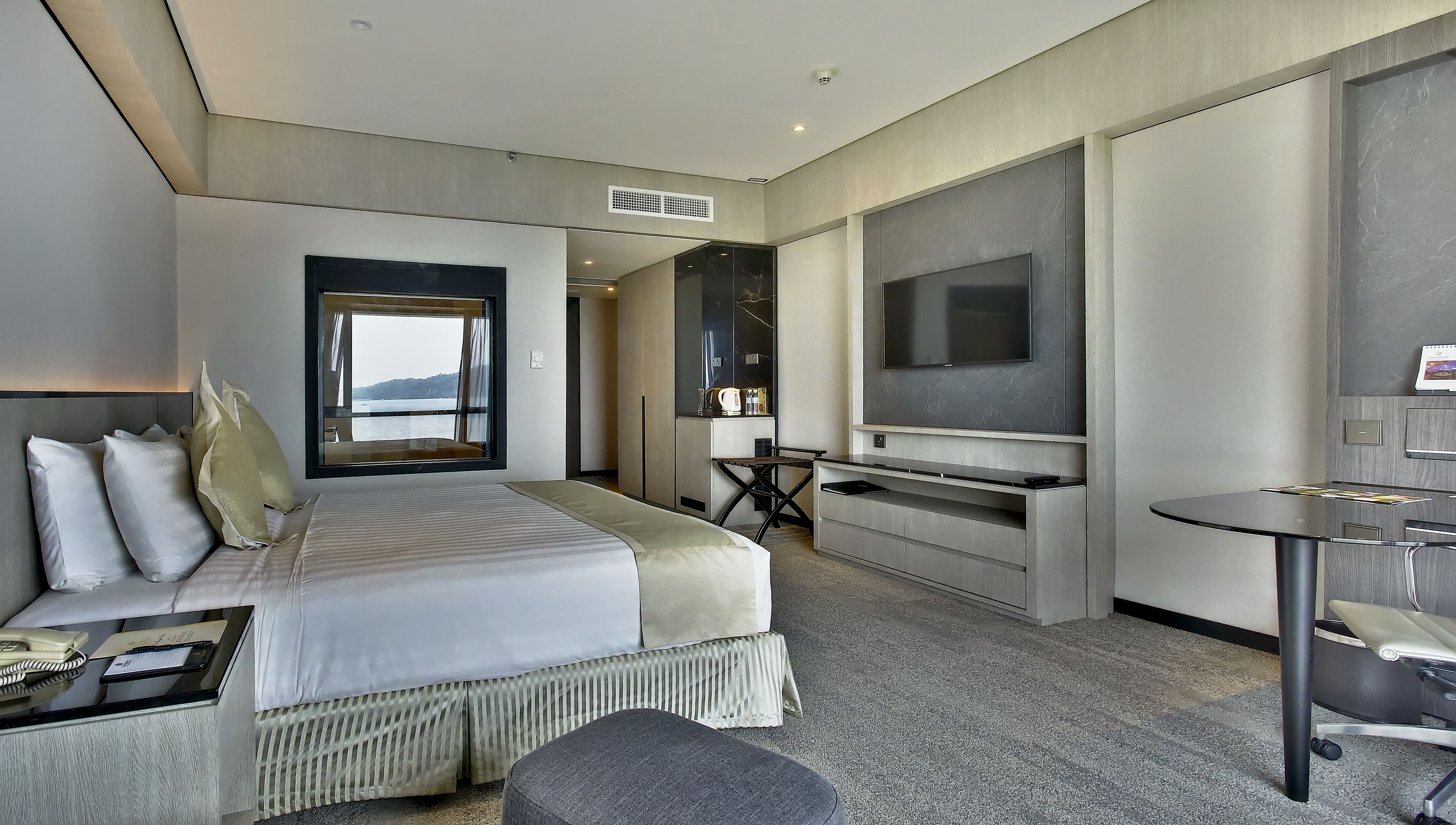 A modern hotel room with a large bed, a desk, a TV, and a view of the outdoors.