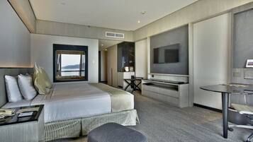 A modern hotel room with a large bed, a desk, a TV, and a view of the outdoors.
