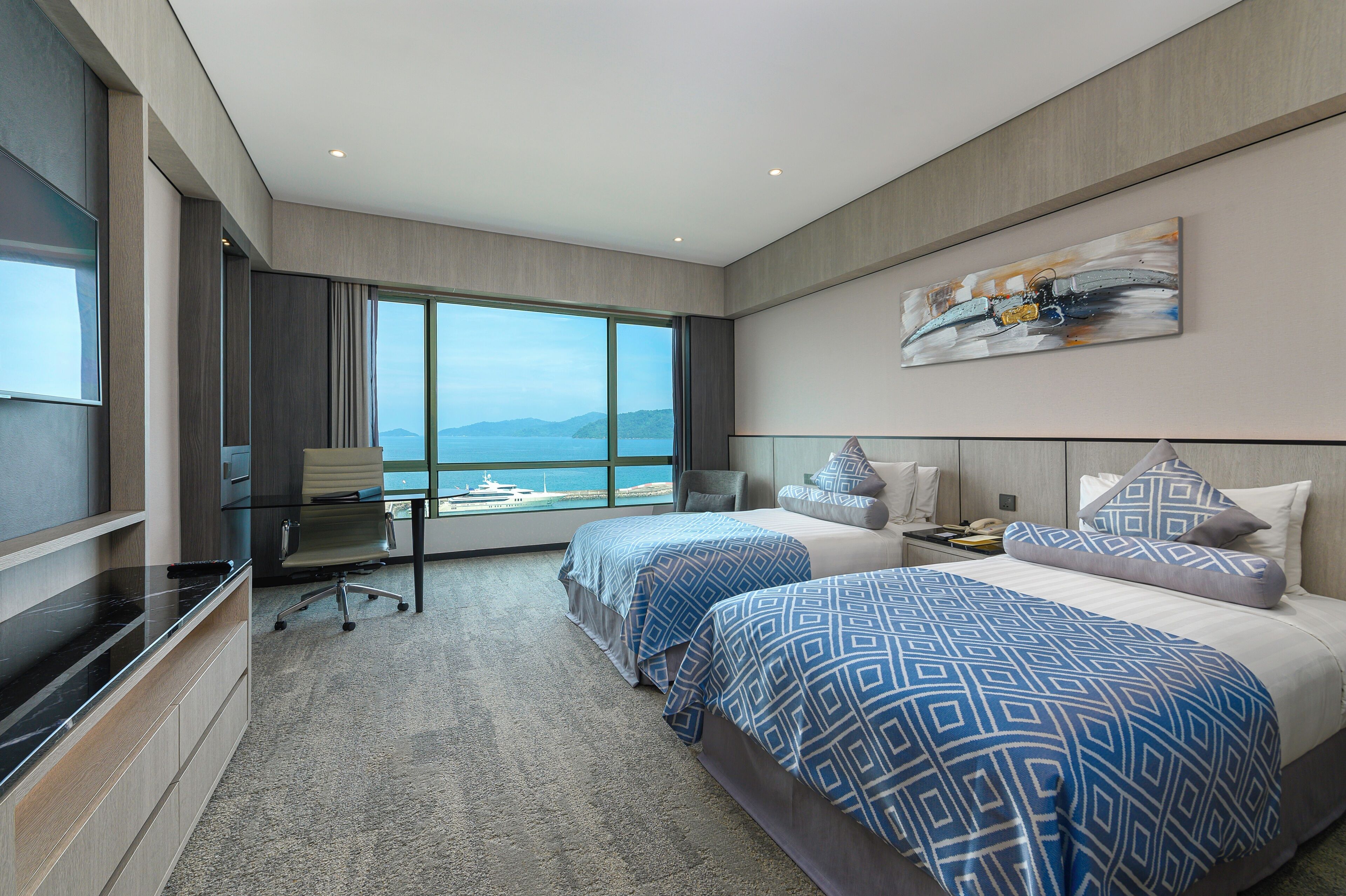 Een moderne hotelkamer met twee bedden, een bureau en een groot raam met uitzicht op zee.