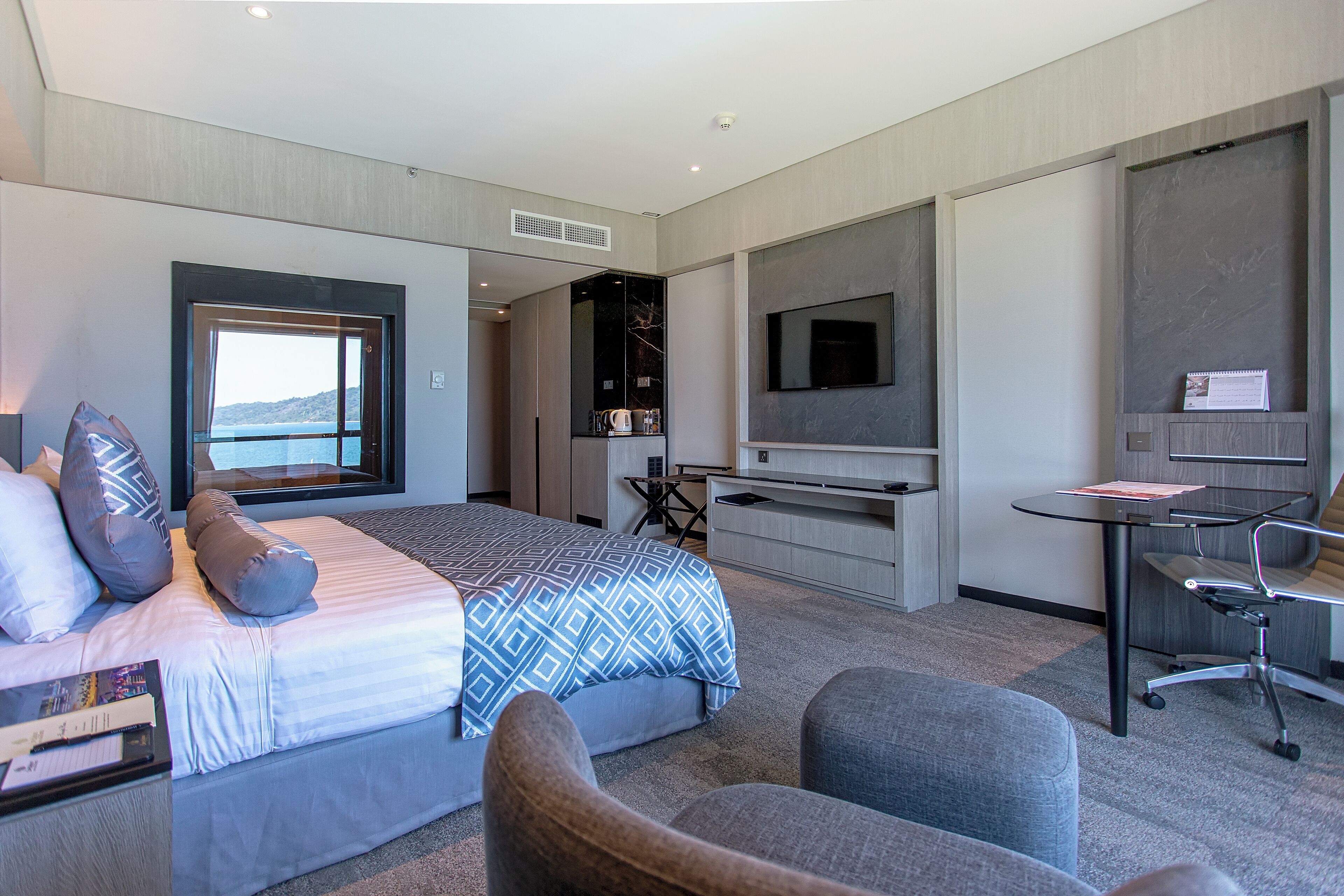 Ein modernes Hotelzimmer mit einem großen Bett, einem Schreibtisch, einem Sessel, einem Fernseher und Meerblick.