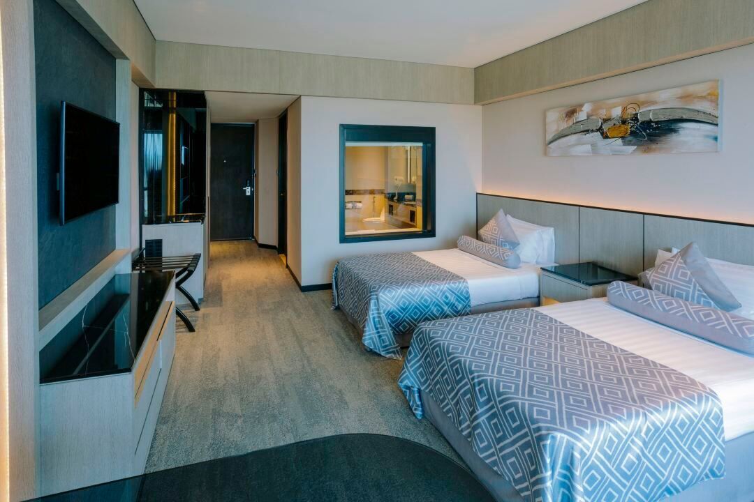 Habitación de hotel con dos camas, televisión, baño con espejo y un cuadro en la pared.