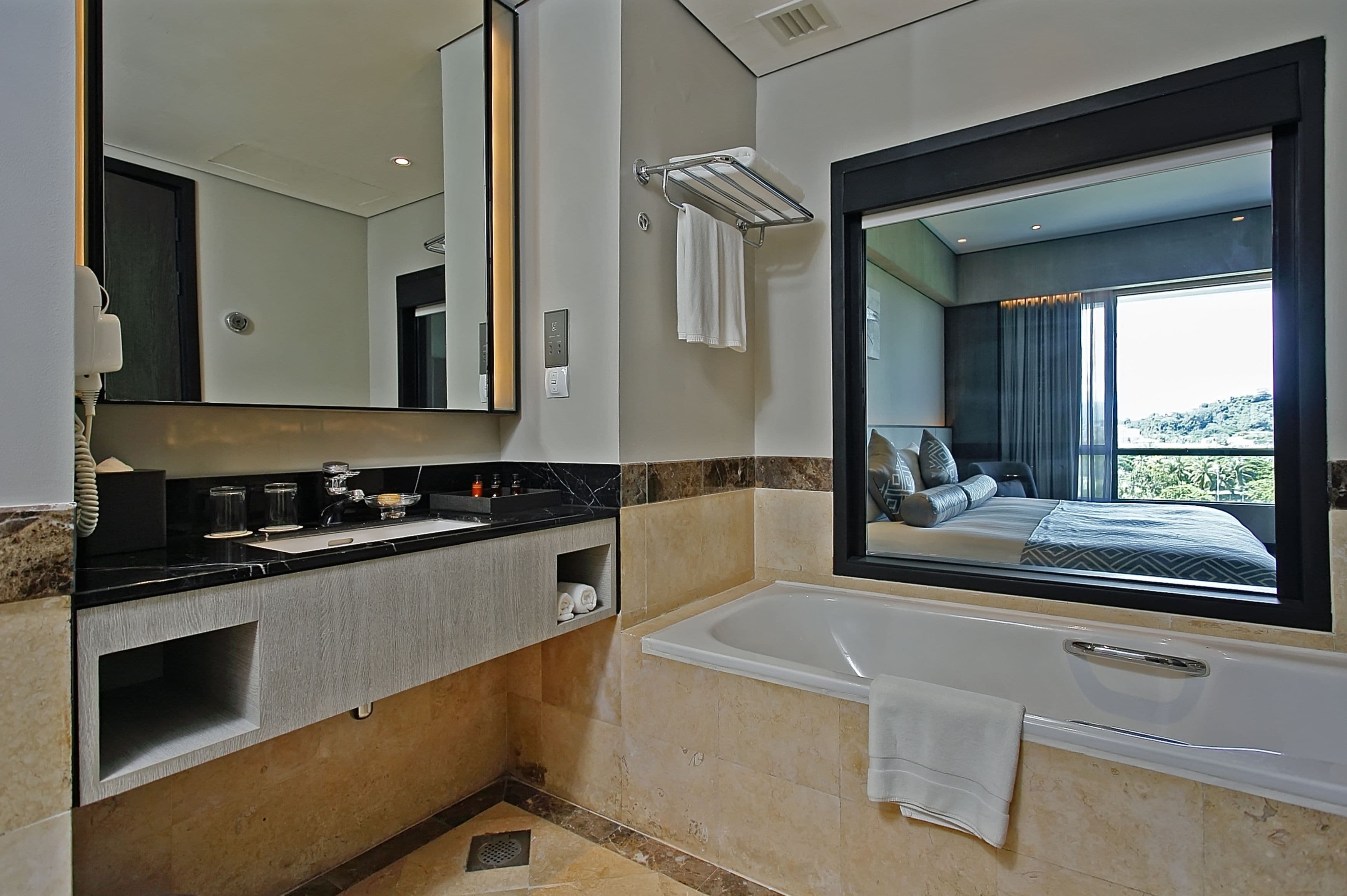 A modern bathroom with a large mirror, a bathtub, and a vanity with a sink and towel rack.
