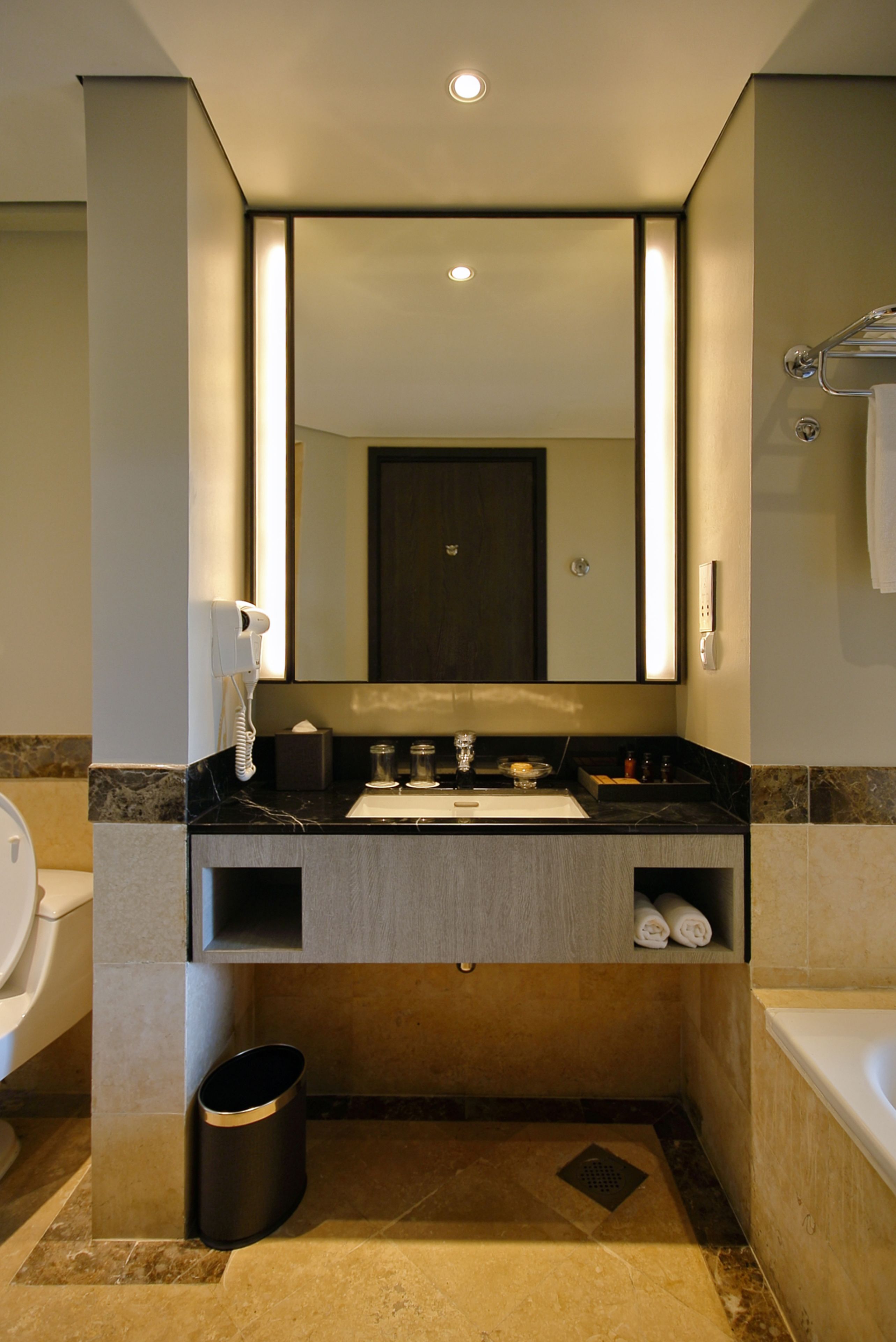 A modern bathroom with a large mirror, a sink, a toilet, and a bathtub.