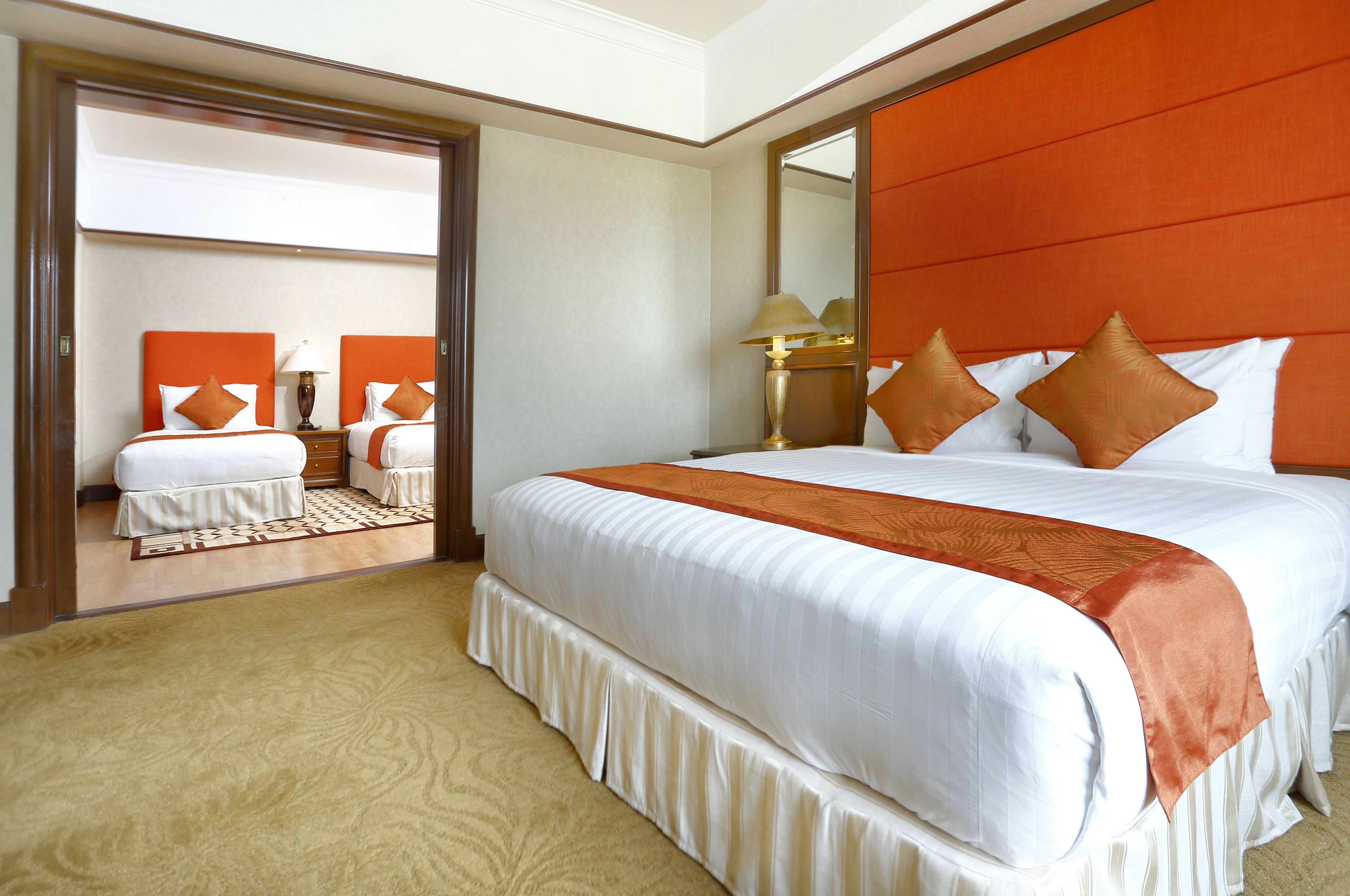A hotel room with a large bed, a mirror, and a view of another room.