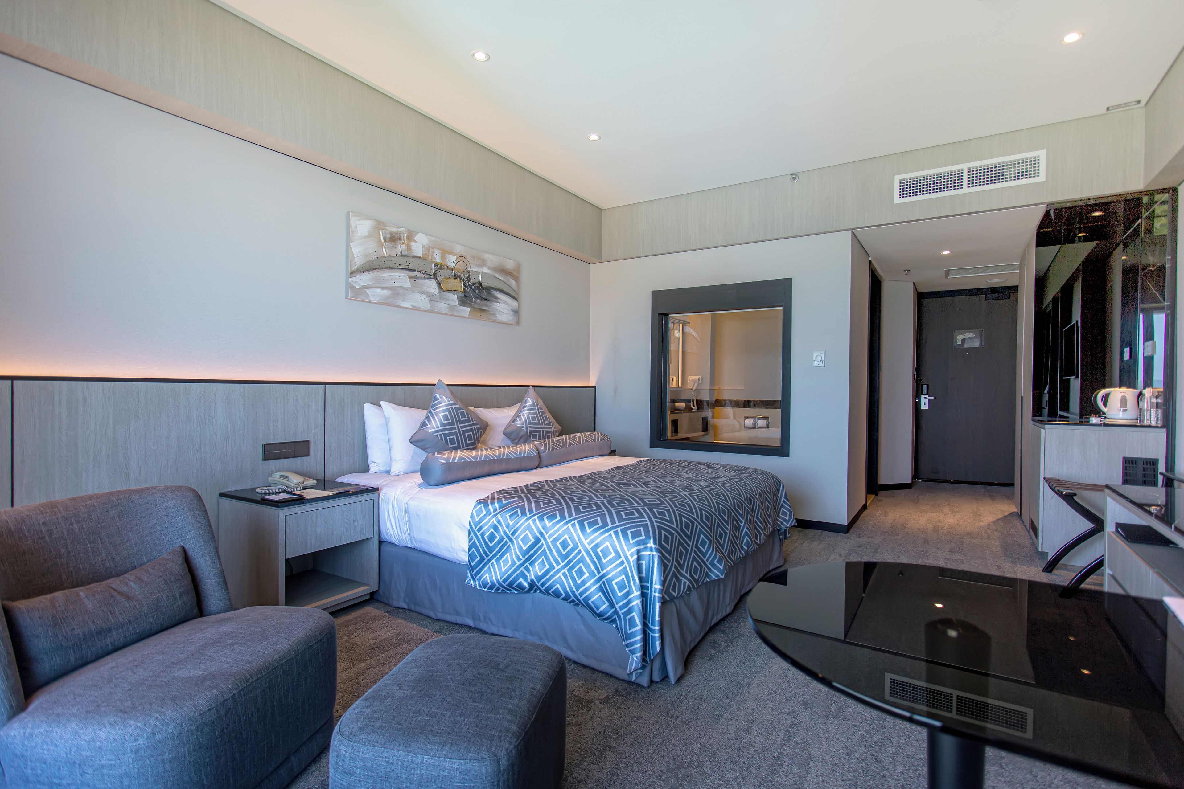 A modern hotel room with a large bed, a desk, a chair, and a mirror.
