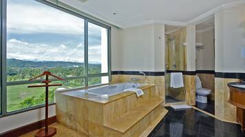Un baño moderno con una bañera grande, una ducha y un inodoro. Cuenta con un ventanal que ofrece vistas a un paisaje verde.