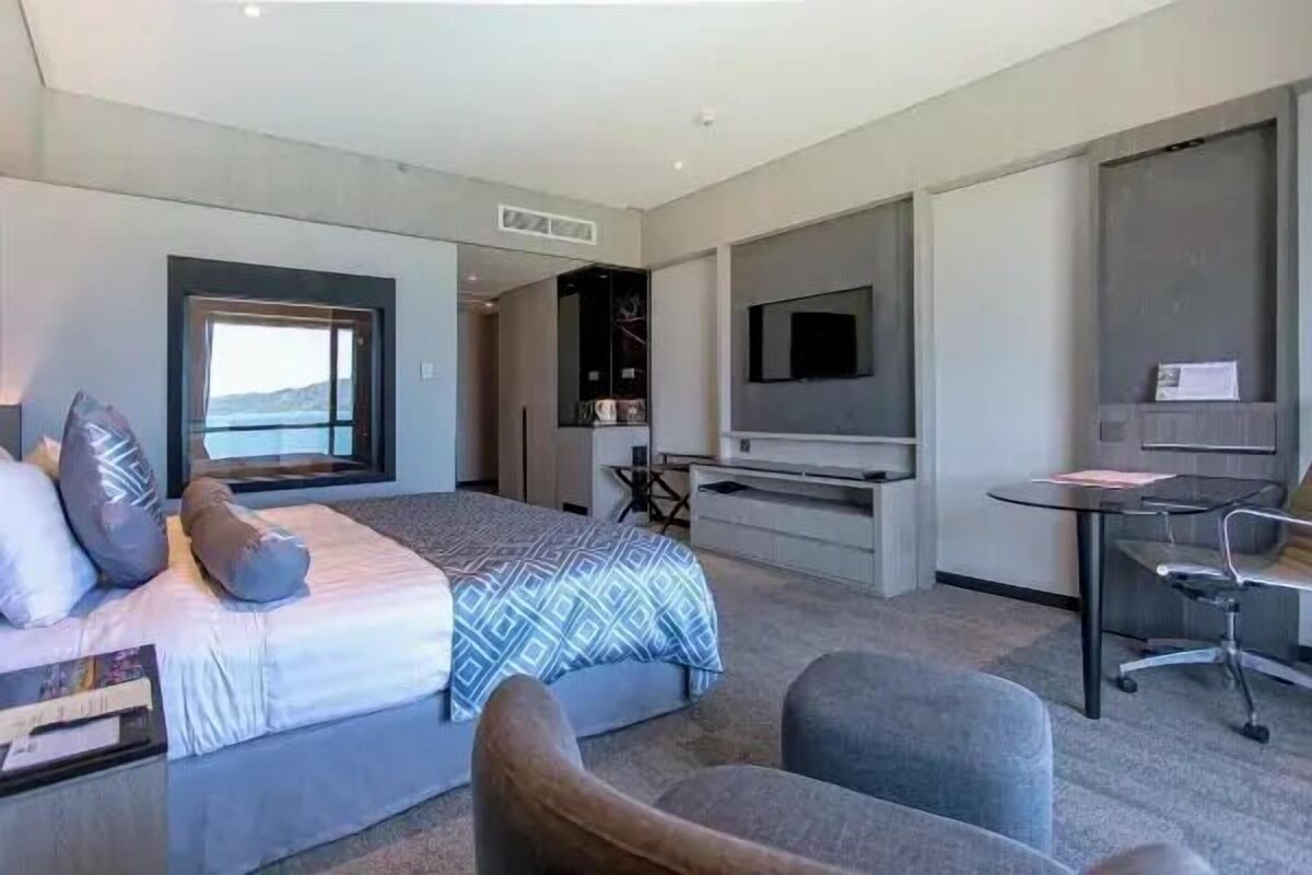 A modern hotel room with a bed, seating area, desk, and a large TV.