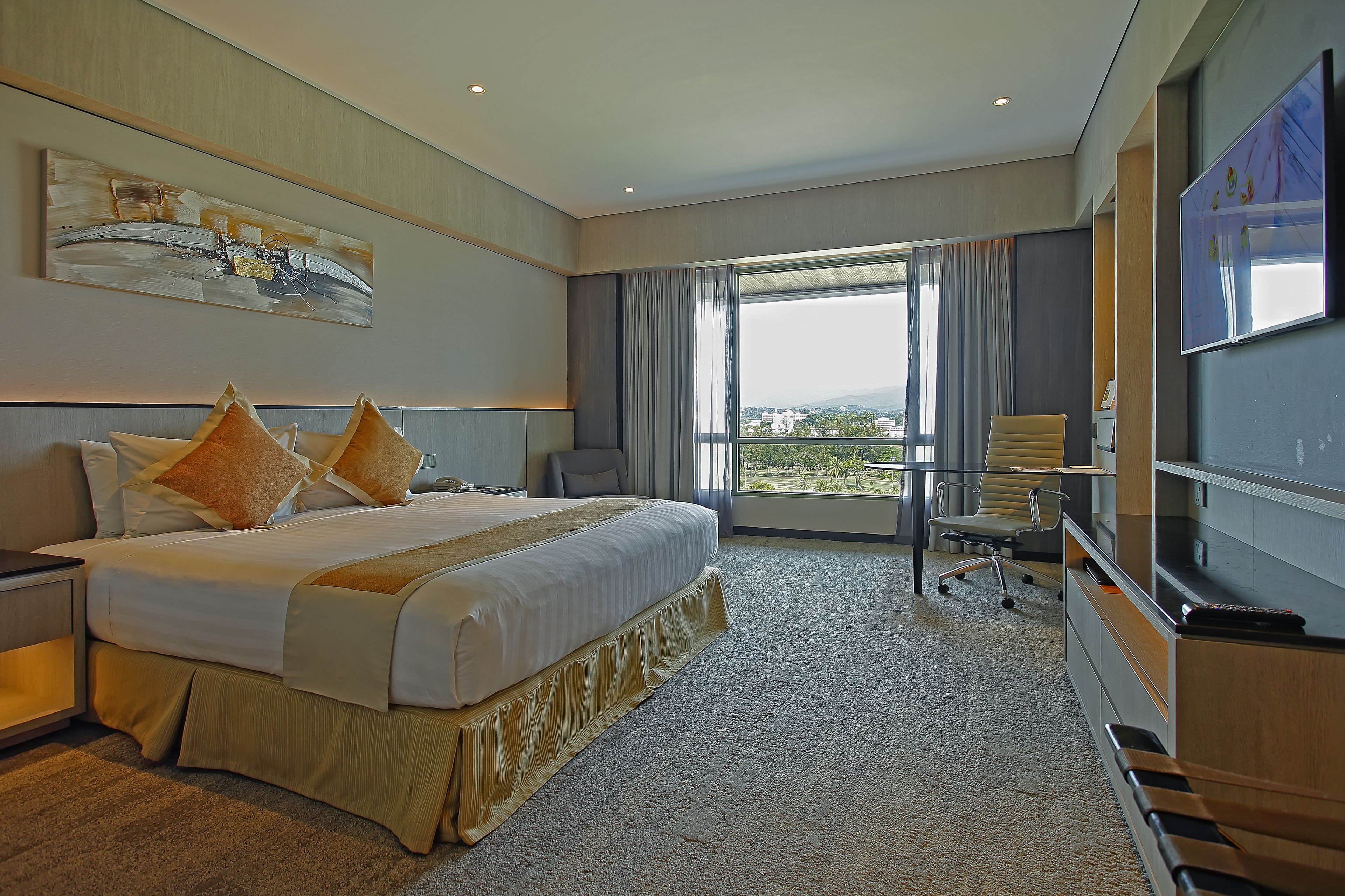 A modern hotel room with a large bed, a desk, a chair, and a TV.