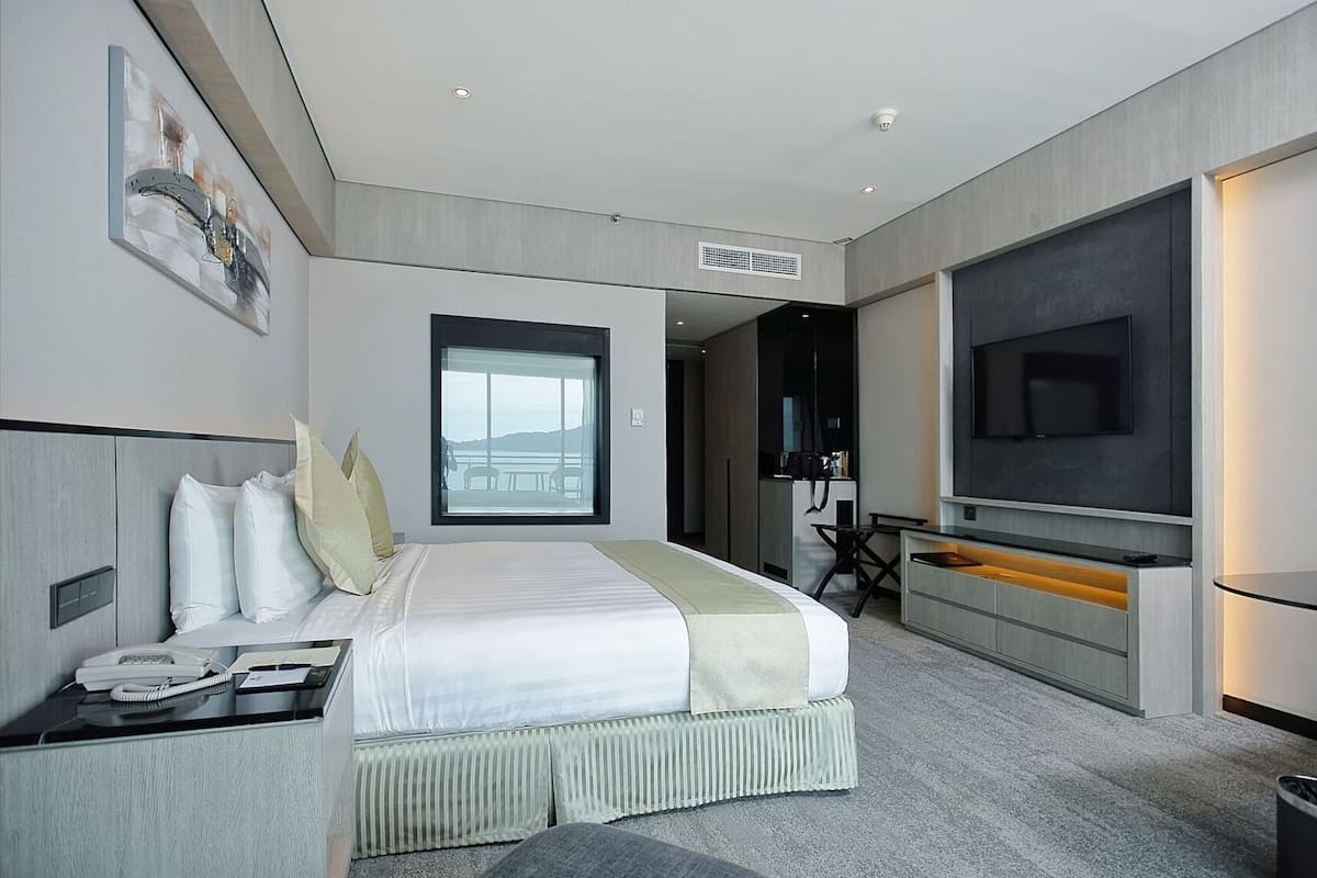 A modern hotel room with a large bed, a desk, a TV, and a view of the outdoors.