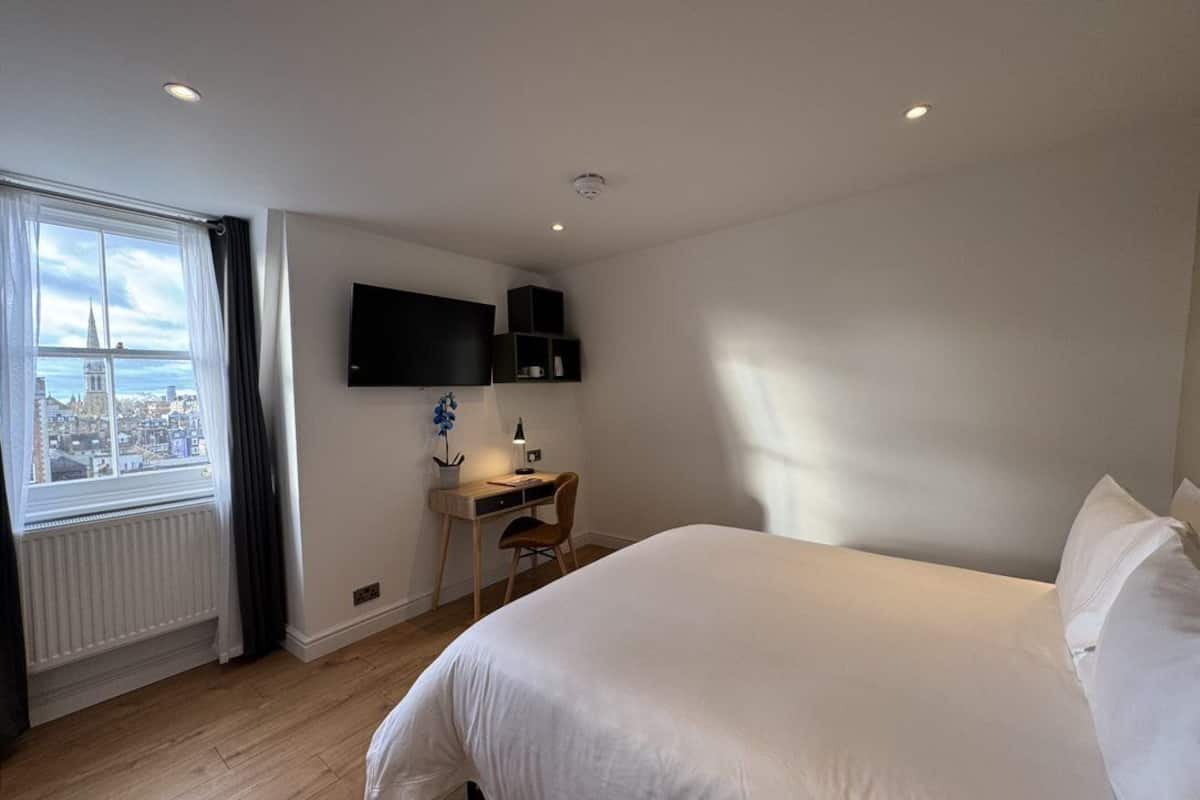 Habitación de hotel con una cama grande, un escritorio con silla, un televisor de pantalla plana montado en la pared y una ventana con vista a la ciudad.
