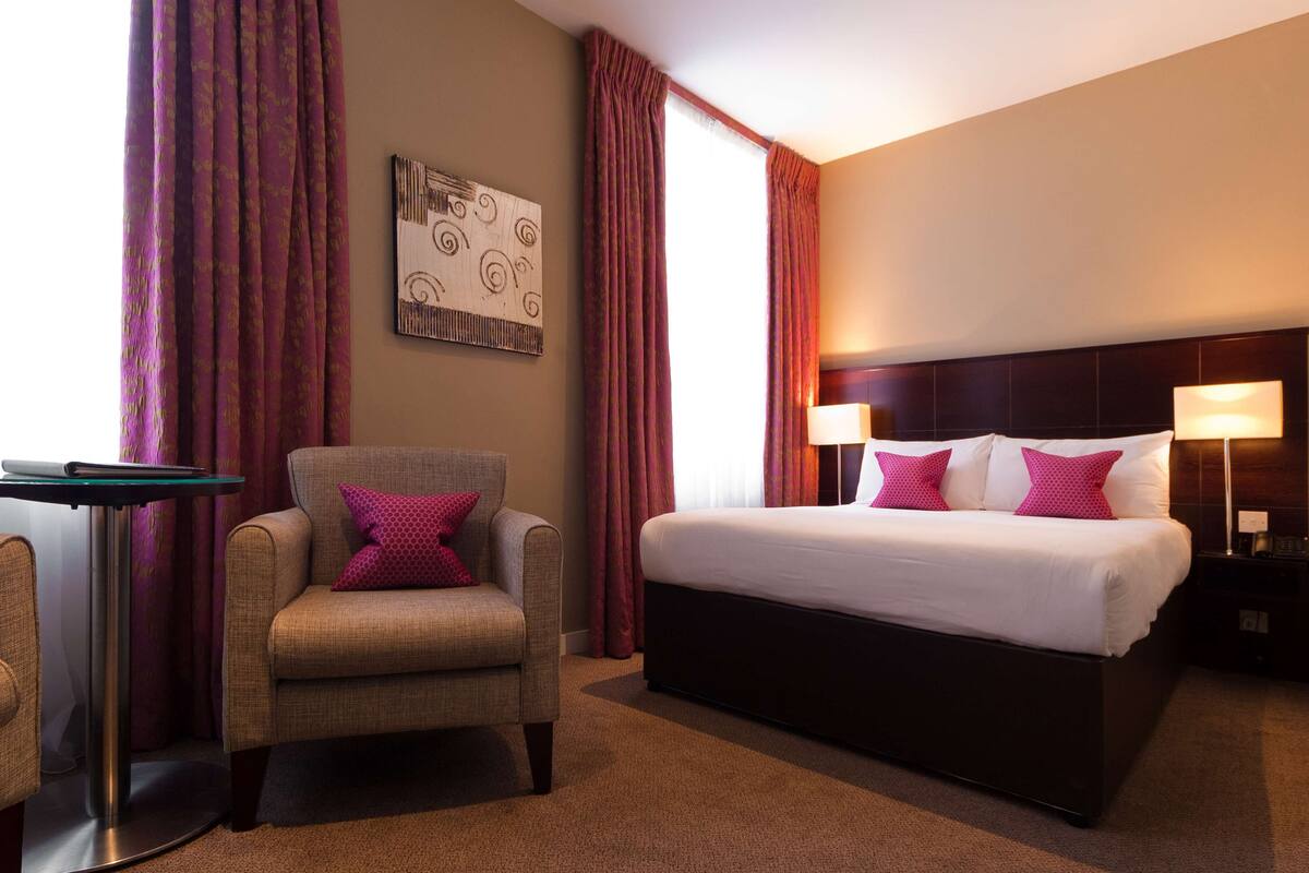 Una habitación de hotel con una cama, una silla, un escritorio y una mesita de noche.