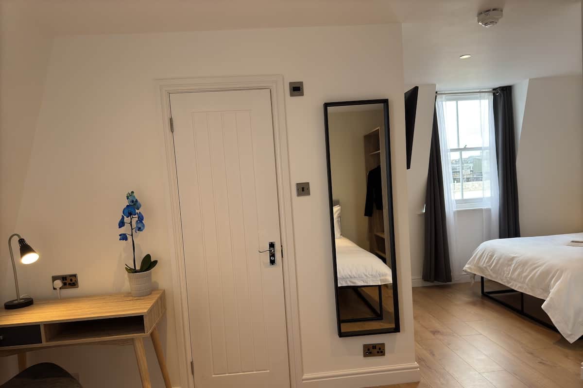 Un dormitorio con escritorio de madera, un espejo, una cama y una ventana con cortinas.