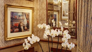 Una habitación con dos cuadros enmarcados, un espejo con lámpara y una mesa con una orquídea en maceta.