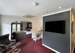 Quarto de hotel moderno com cama, escrivaninha, televisão e área de estar.