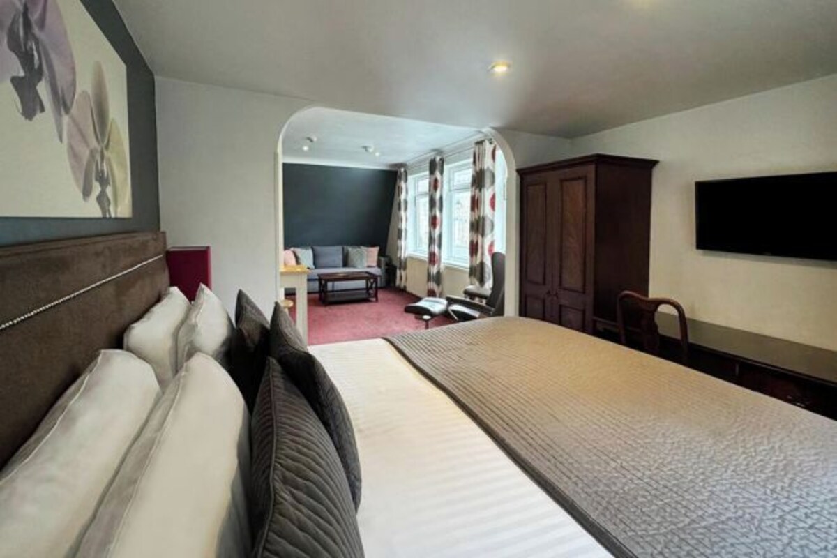 Une chambre d’hôtel avec un grand lit, un bureau, une chaise, une armoire et un téléviseur fixé au mur.