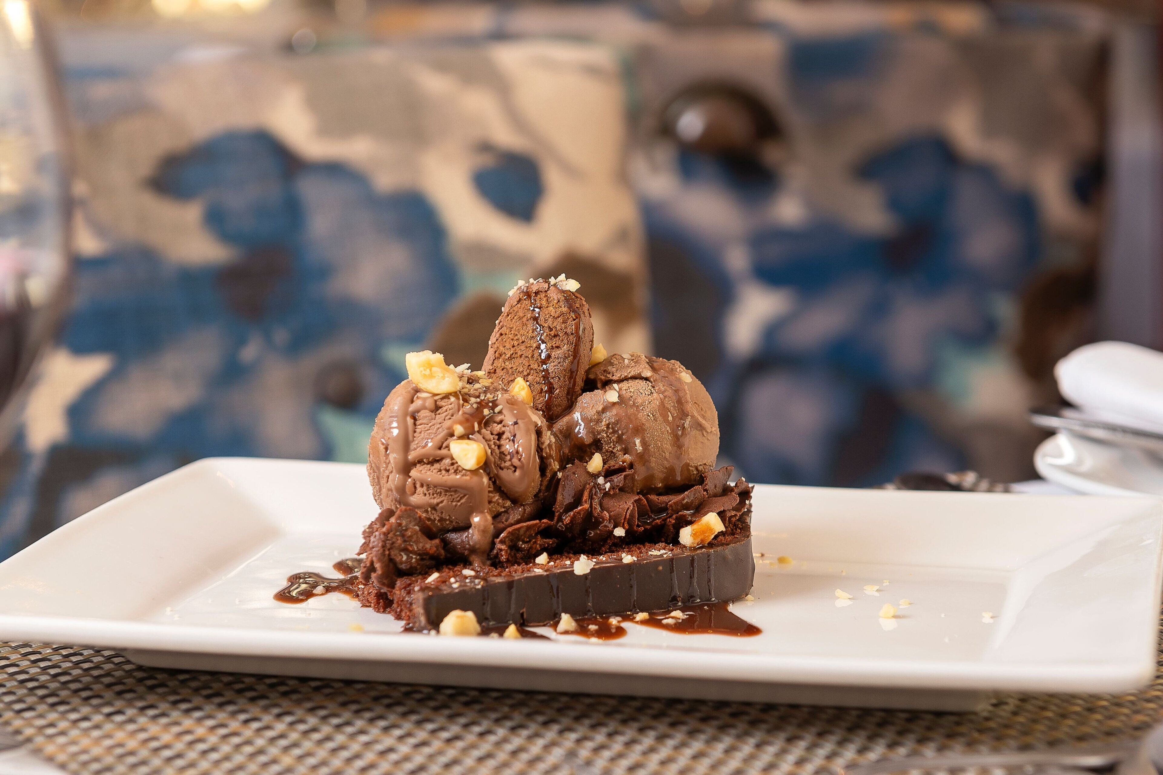 A dessert plate with chocolate ice cream and nuts on a white plate.