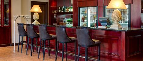 Zona de bar con cuatro taburetes altos, una caja registradora y una variedad de botellas y vasos en estanterías.