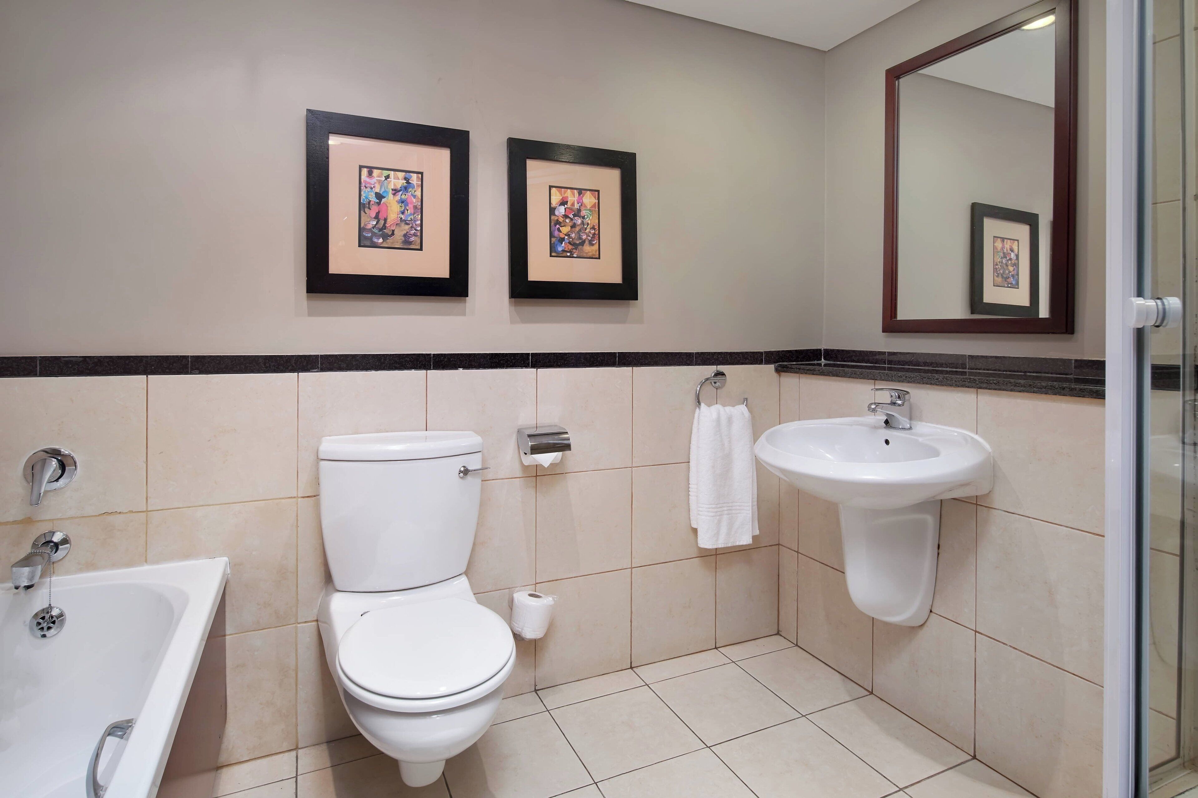 A bathroom with a toilet, sink, and bathtub. There are two framed pictures on the wall.