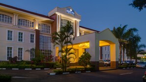 A hotel with a prominent entrance, a covered waiting area, and a parking lot with several cars.