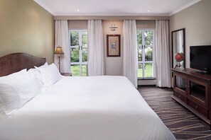 Una habitación de hotel con una cama grande, televisión, cómoda de madera y ventana con cortinas.