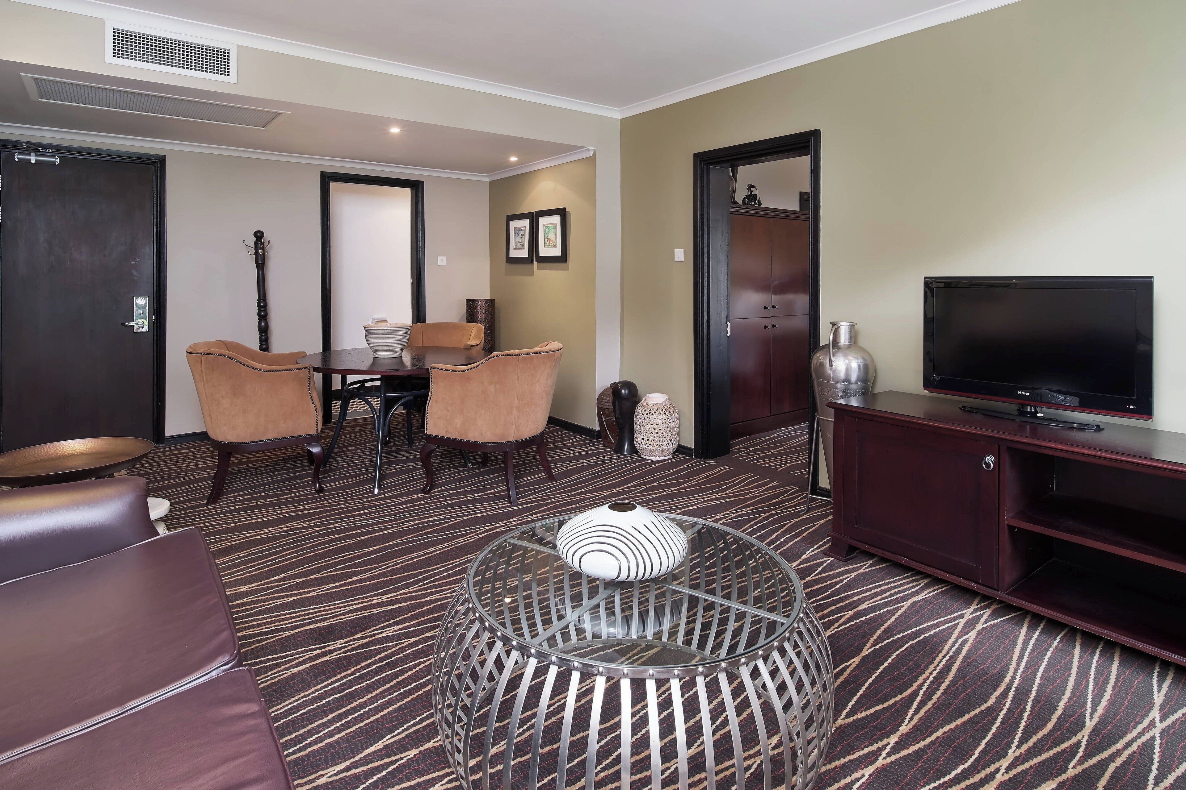 A hotel room with a dining area, a TV, and a decorative glass table.