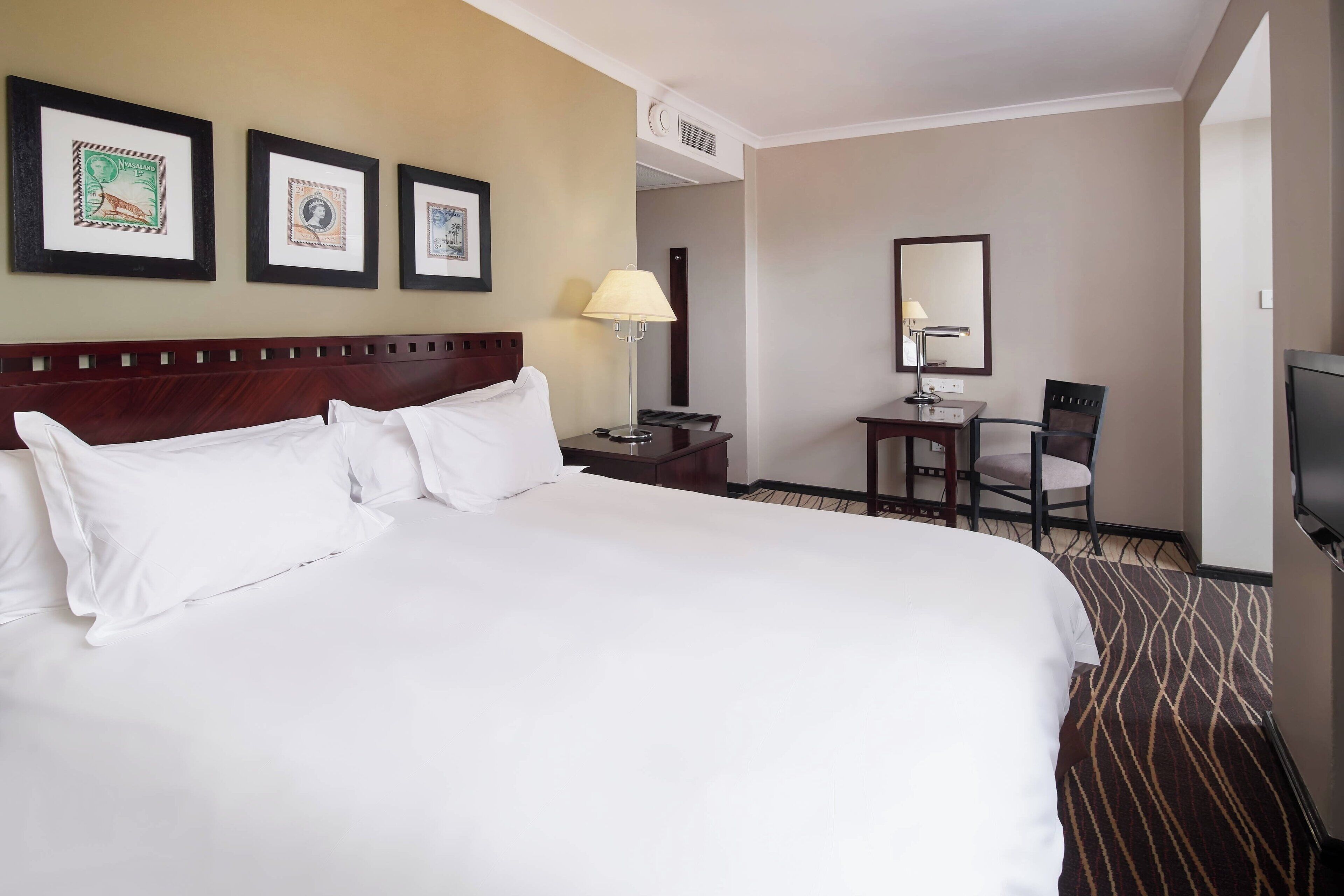 Een hotelkamer met een groot bed, een bureau met stoel, een televisie en ingelijste foto's aan de muur.
