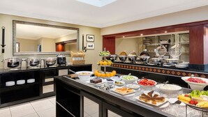 A buffet setup with various food items and a large mirror on the wall.
