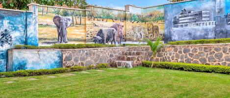 A mural of wildlife on a stone wall with a grassy area in front.