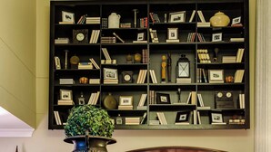 A reception area with a wooden reception desk, a large bookshelf filled with books and decorative items, and a view into a dining area with tables and chairs.