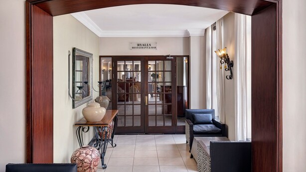 A hallway leading to a restaurant and bar with a wooden archway, a vase, a table, and a sofa.