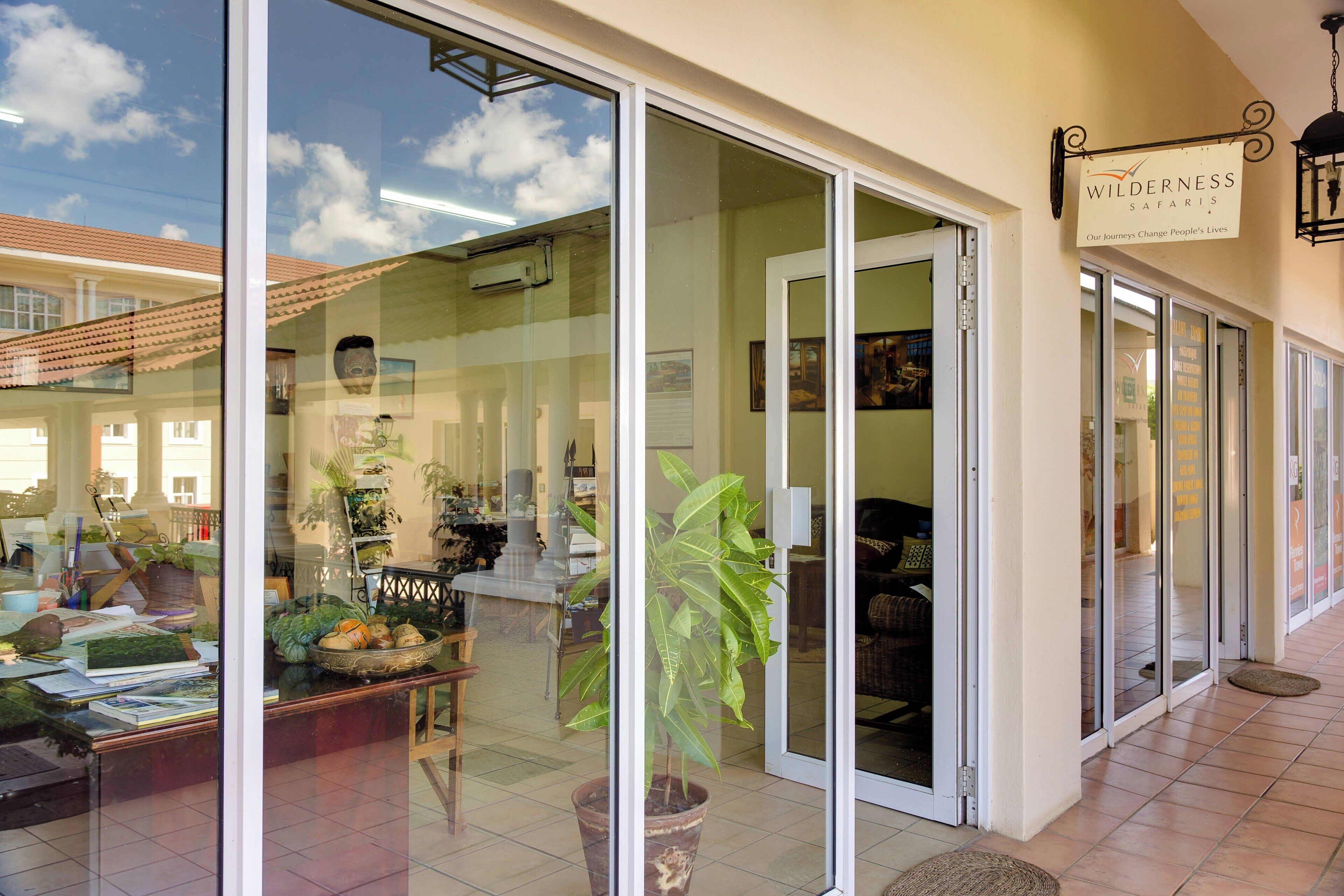 A hotel lobby with a large glass door, a sign reading "Wilderness Safaris," and a potted plant in the center.