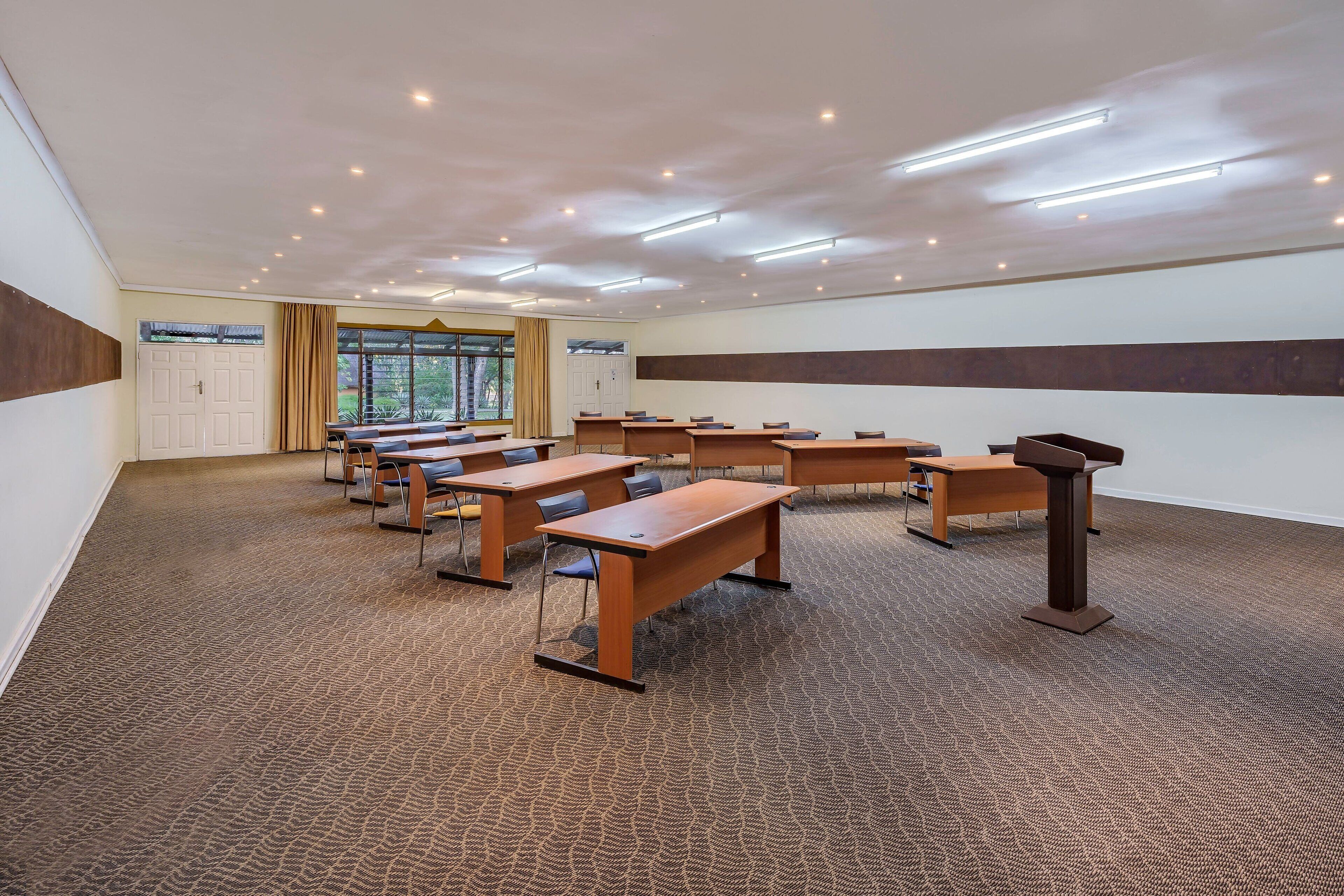 A conference room with multiple tables and chairs, a podium, and a large window with curtains.